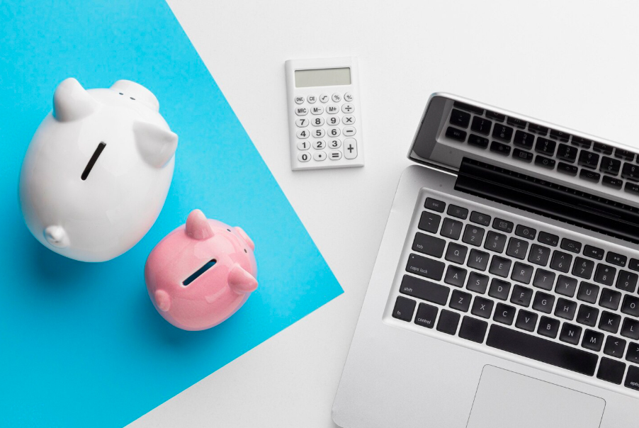 Calculatrice et tirelires cochons près d'un ordinateur portable.